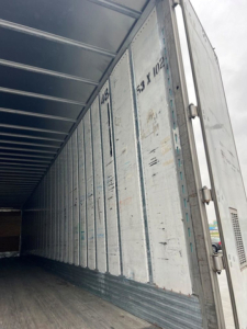 Interior of an open utility van trailer showing corrugated metal walls and ribbed ceiling with vertical door hinges.