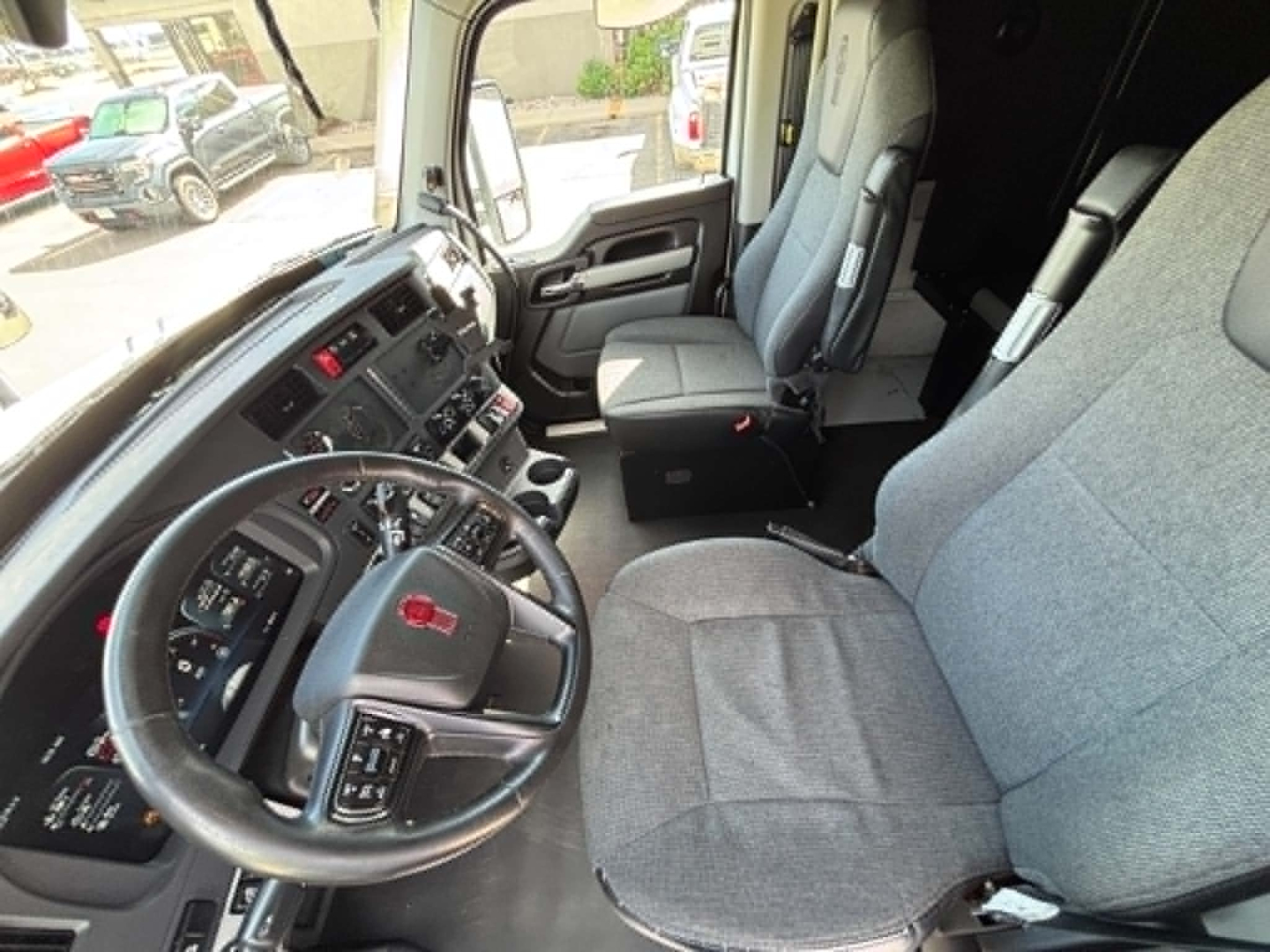 Cab interior of a 2023 Kenworth T680 showing steering wheel, driver's seat, and dashboard in view.