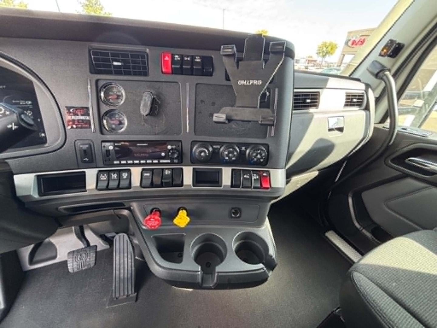 Dashboard and center console of 2023 Kenworth T680 showing gauge cluster, controls, cup holders, and mounting for a Garmin device.