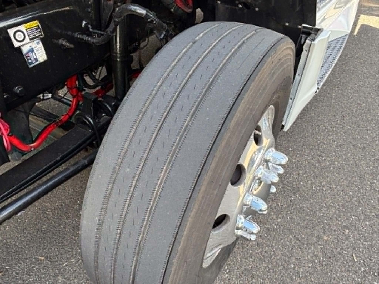 Kenworth T680 wheel and front suspension with dual rear axle lug nuts and treaded tire; visible engine bay components and red hoses.