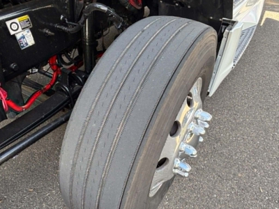 Kenworth T680 wheel and front suspension with dual rear axle lug nuts and treaded tire; visible engine bay components and red hoses.