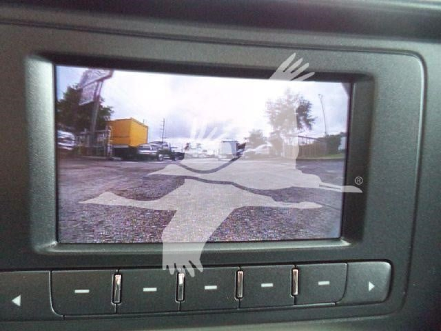 Rearview camera display showing a truck yard with a yellow trailer and other vehicles, Silverado 6500HD listing context text overlay.