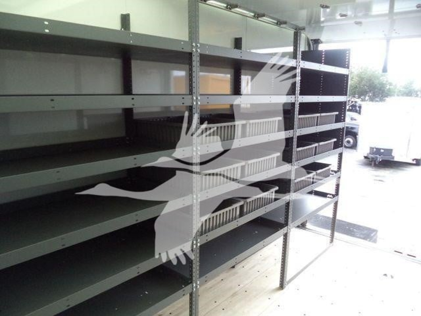 Shelving racks inside a utility trailer or showroom with multiple empty gray metal shelves