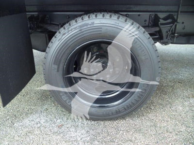 Wheel/axle area of a box truck showing a single tire with rim and suspension components visible.