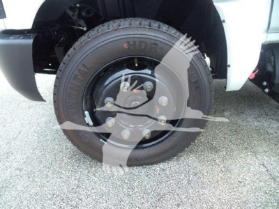 Truck wheel and hub area showing a black steel rim with lug nuts on a Silverado chassis; tire tread visible and white body panel above; partial suspension and brake components.