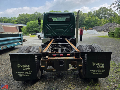 Truck chassis rear view showing dual rear axles and Viking Cives mud flaps, cab missing, metal frame with rust tones and gravel background.