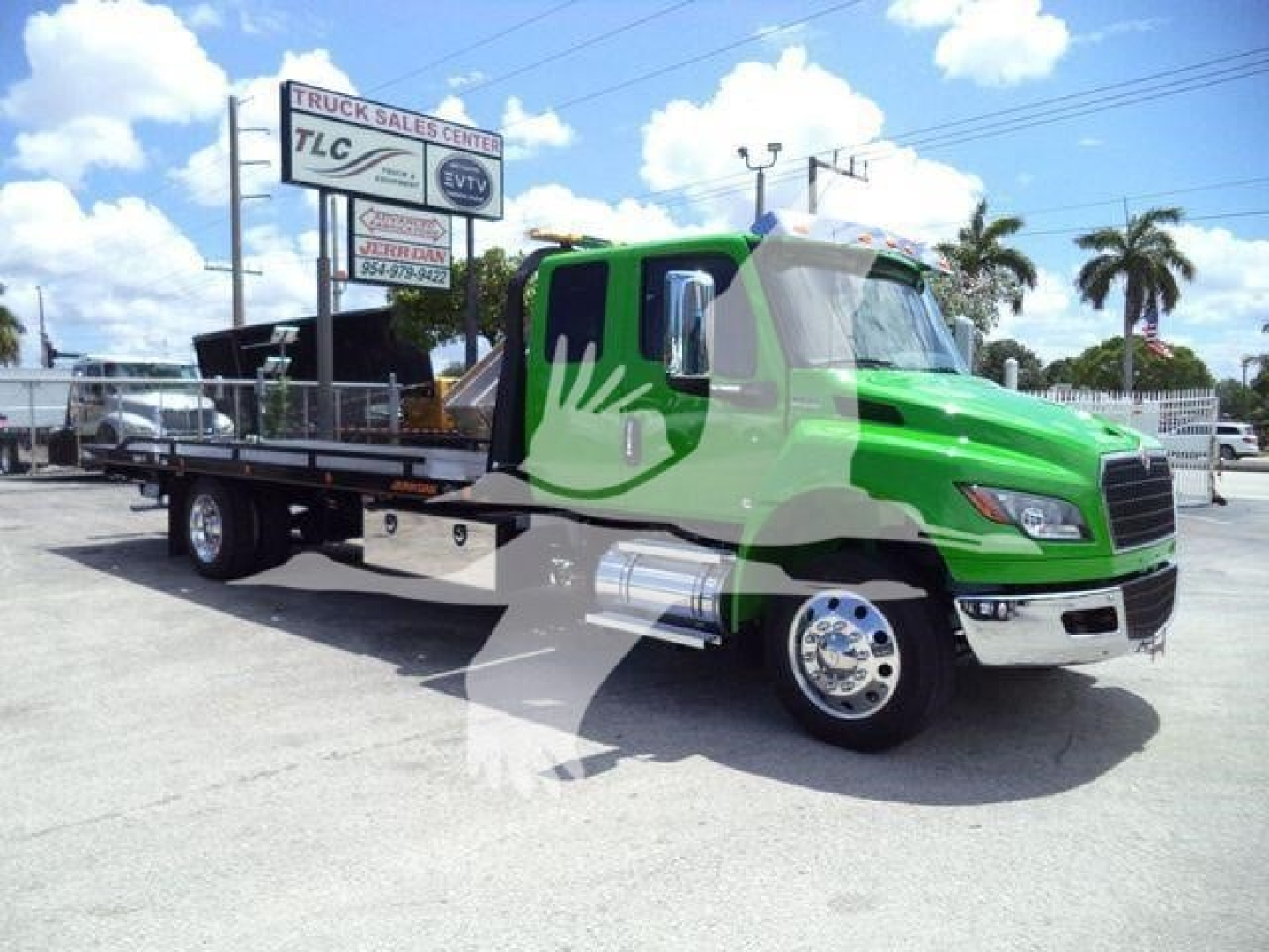 Green International flatbed tow truck in a dealership lot, side view.