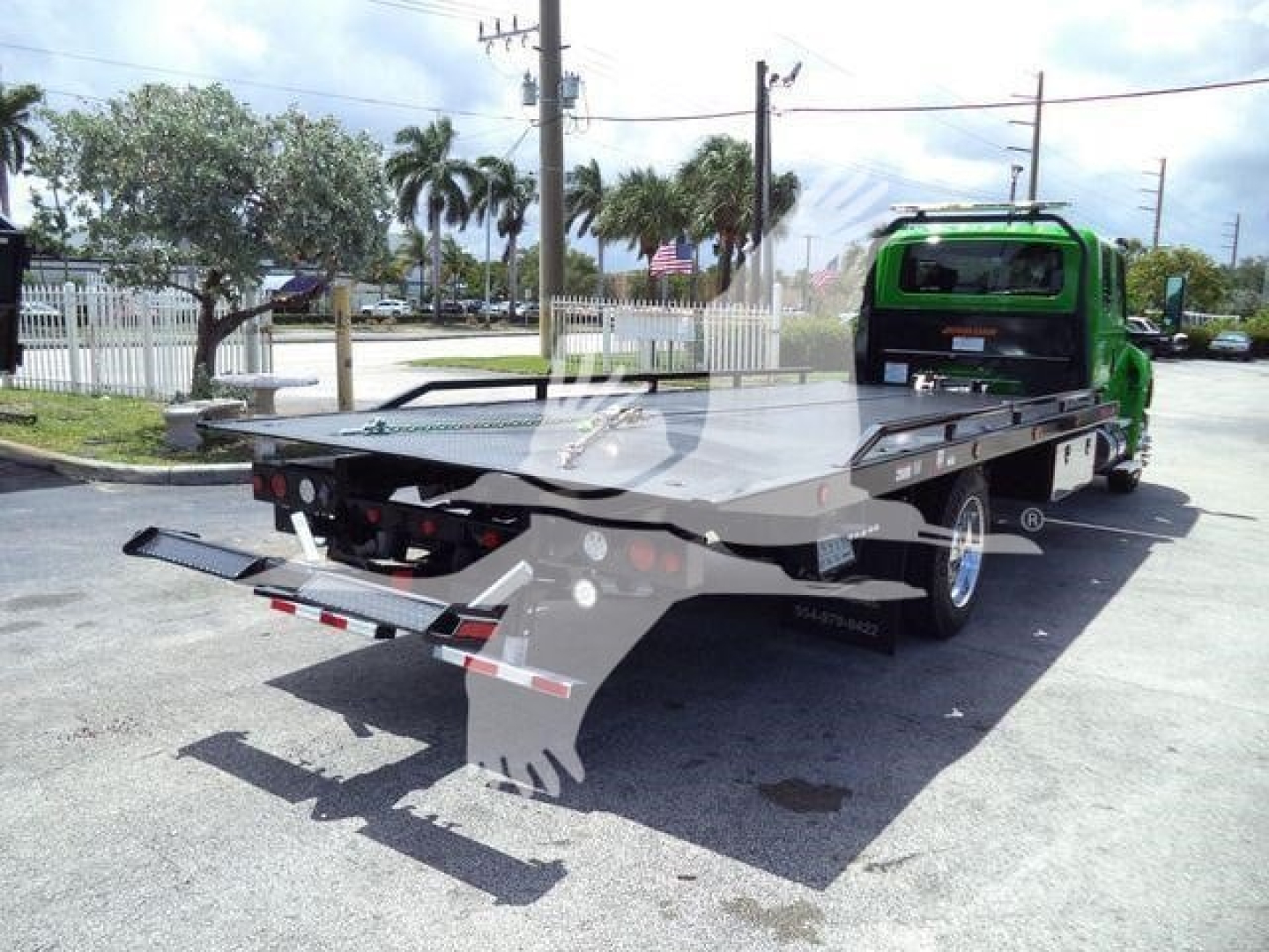 Flatbed tow truck rear view showing rollback with green cab and metal deck, taillight assembly, and rear underride bars.