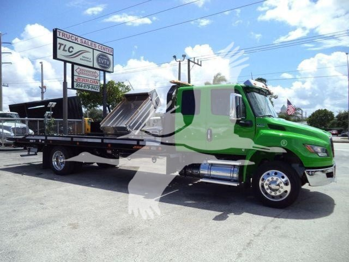 International MV rollback truck with a green cab and flatbed in a dealership lot, stock number J24111FM, image shows side view of the truck.
