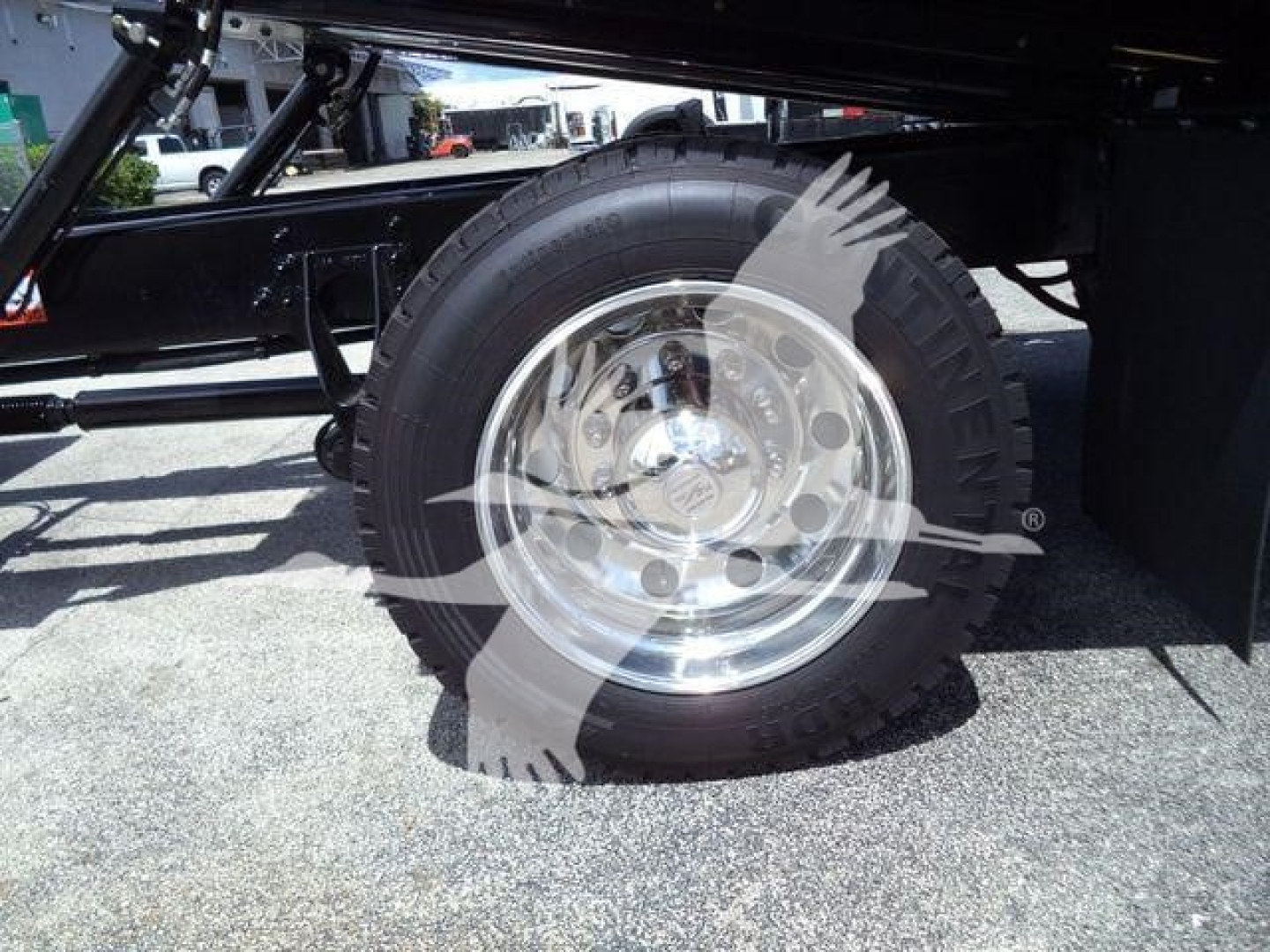 Wheel and tire of a heavy-duty truck undercarriage with polished aluminum rim and black frame; visible tire treads and part of suspension.