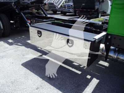 Storage toolbox mounted under a truck bed with two circular vents and a diamond-plate lid, adjacent to a green truck frame.