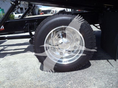 Wheel and tire of a heavy-duty truck undercarriage with polished aluminum rim and black frame; visible tire treads and part of suspension.