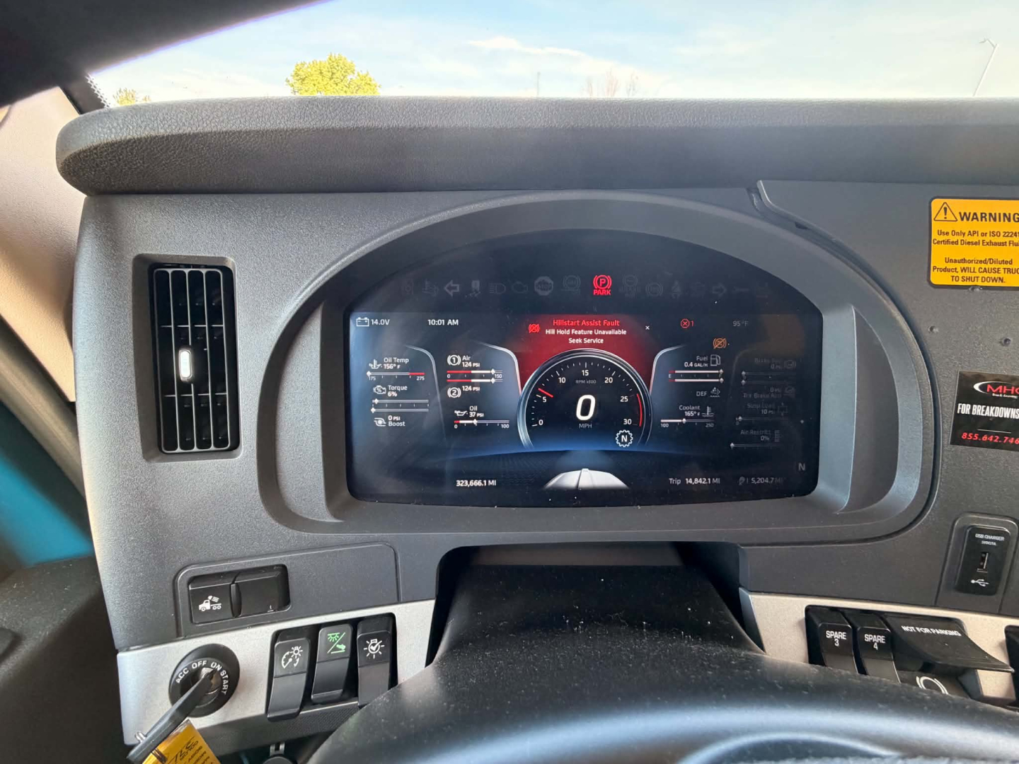 Kenworth T680 interior dashboard displaying digital gauge cluster; left switches panel; warning sticker on right window; steering wheel visible; digital speedometer reads 0 mph.