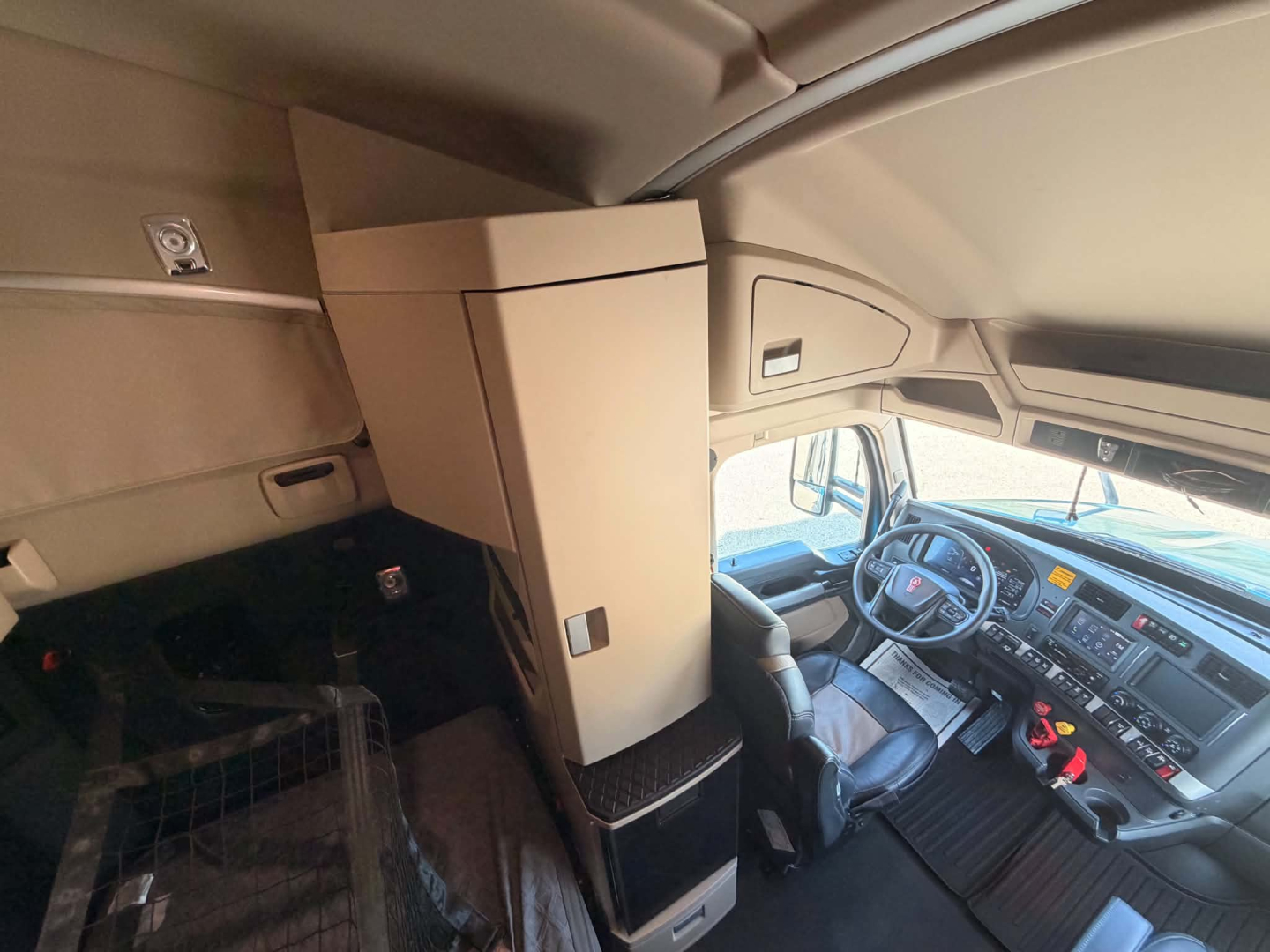 Kenworth T680 truck interior with dashboard and sleeper area visible, including overhead storage cabinet and driver seat.