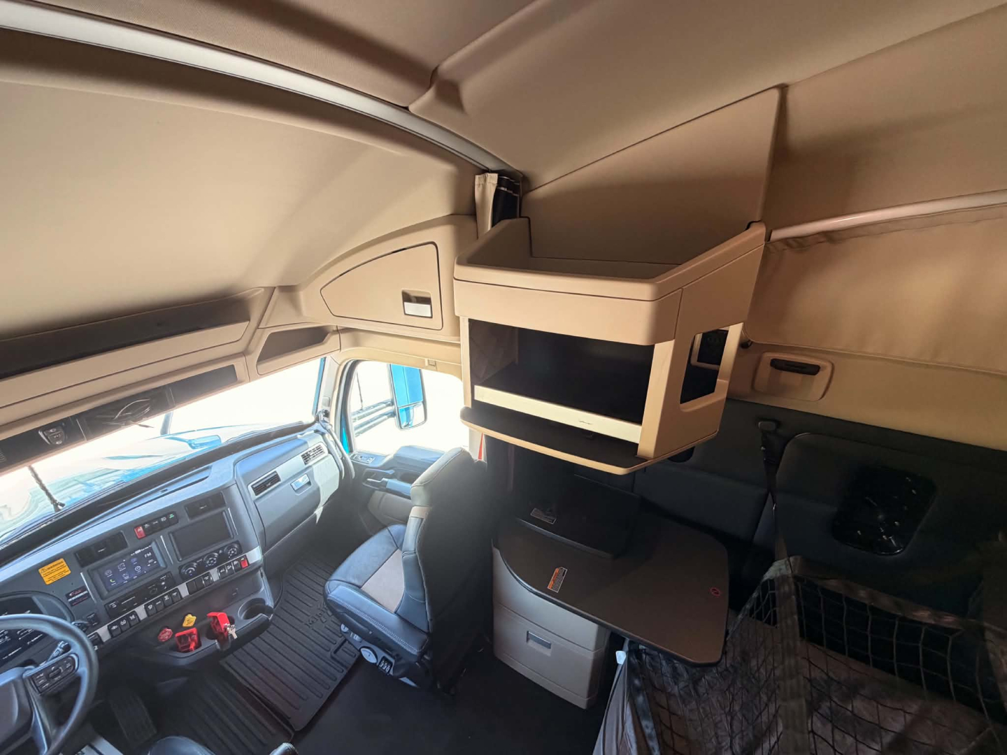 Interior of Kenworth T680 cabin showing overhead storage with fold-out table and mounted screens; driver seat with dashboard controls visible.