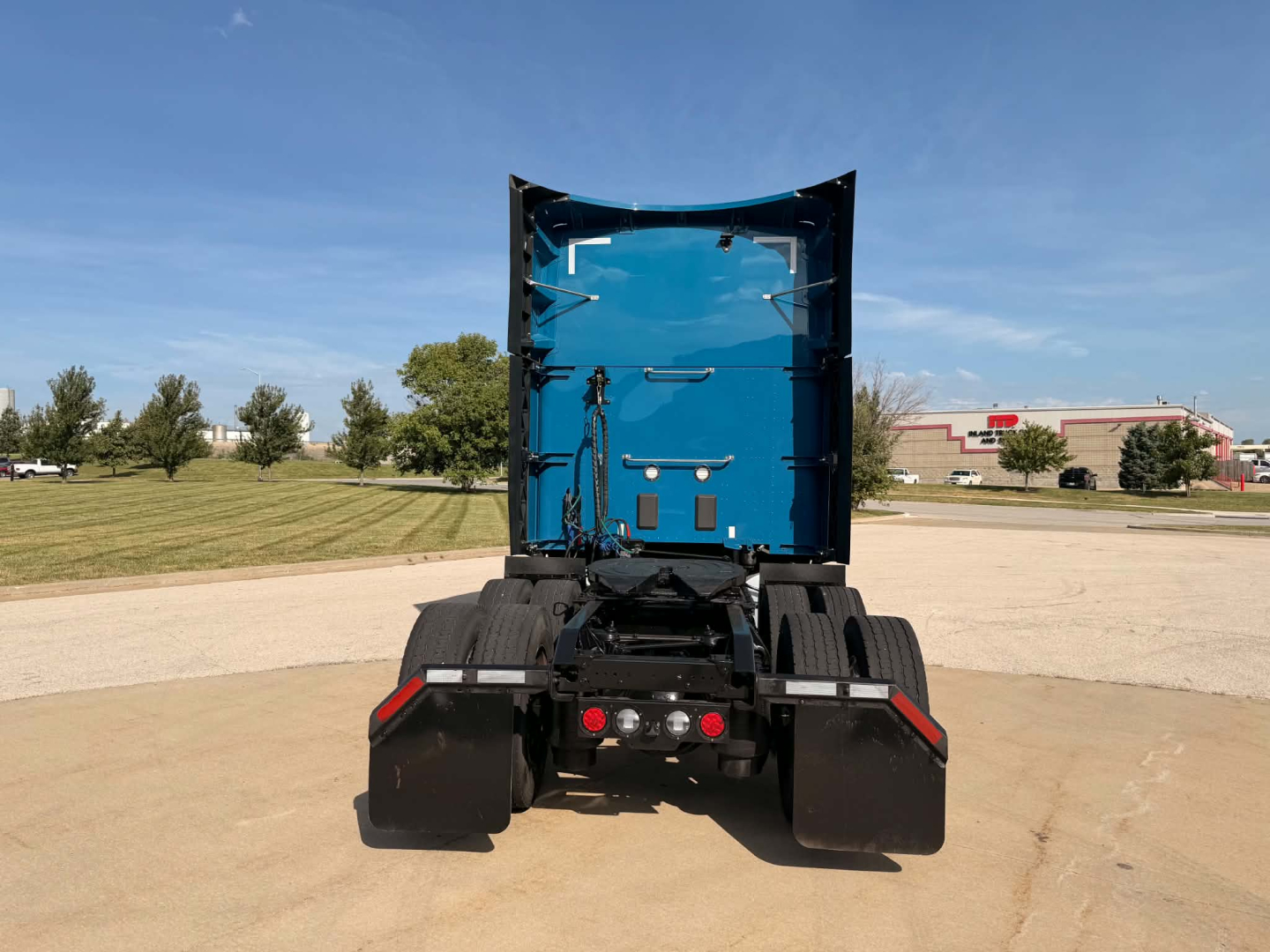 Kenworth T680 rear view showing fifth wheel, rear tires duals, mud flaps, and blue cab interior visible from back.