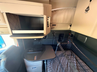 Interior cab of a Kenworth T680 showing a mounted microwave above a fold-out table and a sleeping berth with a cargo net.