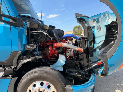 Kenworth T680 engine bay showing exposed red turbo and blue coolant hoses with open hood and wheel visible