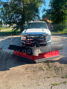 Ford F-350 pickup truck with a large red snow plow attached in front, service/utility truck, white cab, daytime outdoor lot.