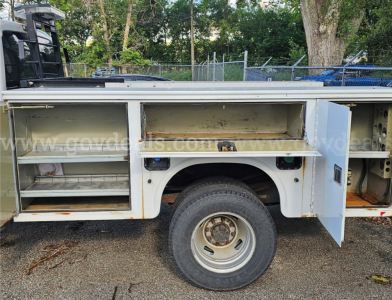 Ford F-350 service body side compartments with open tool/storage drawers and wheel visible; white utility truck bed; stock number and VIN partially shown in listing.
