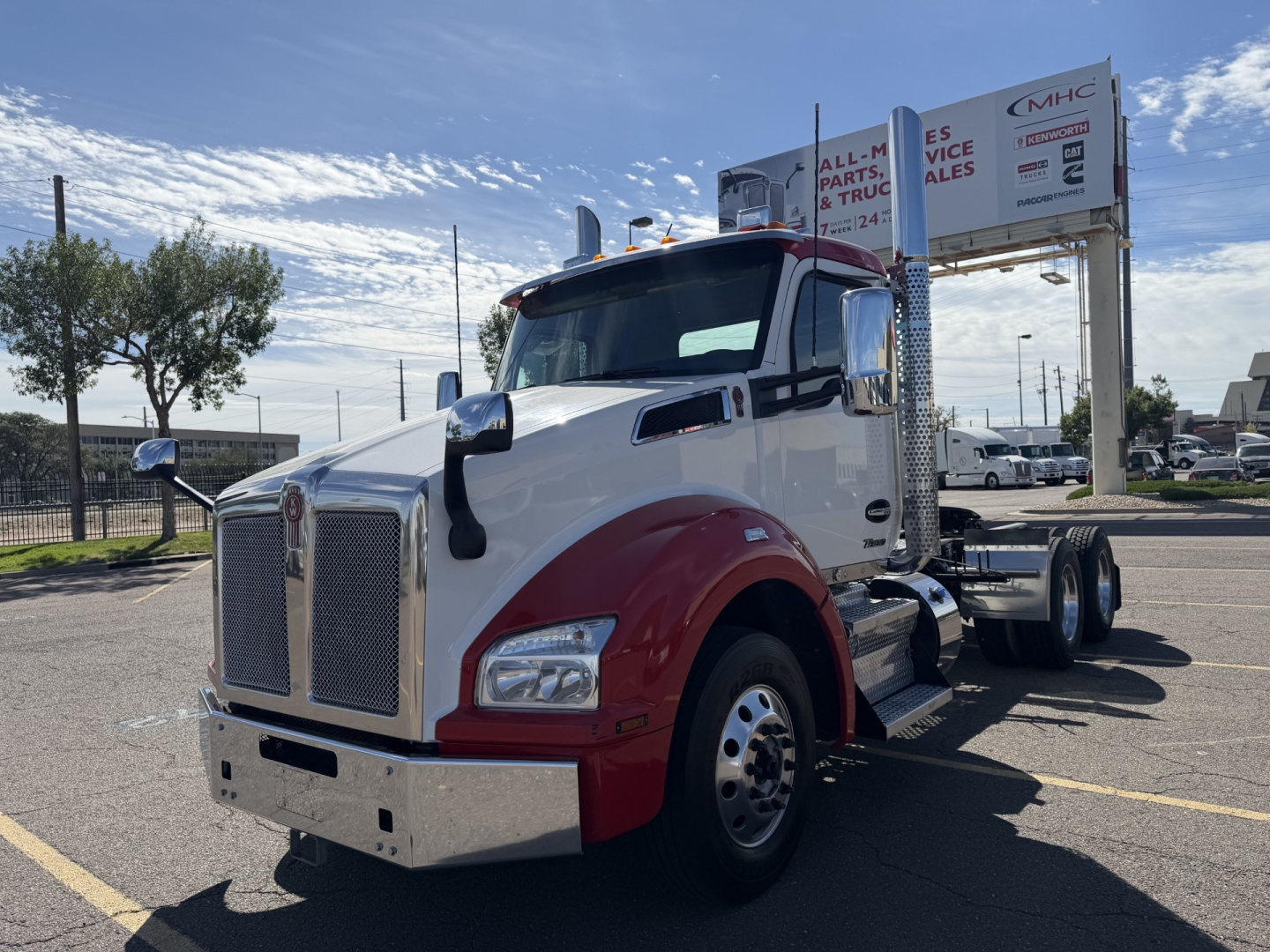 Kenworth T880 conventional daycab truck in white and red two-tone, front grille and large chrome bumper, dual rear axles and chrome mirrors visible in dealership lot.