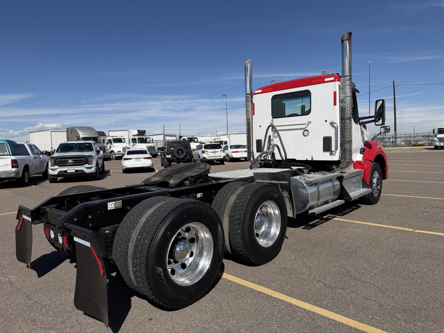 Kenworth T880 daycab tractor with red and white cab, dual rear axles, chassis, and fuel tanks in an outdoor lot.