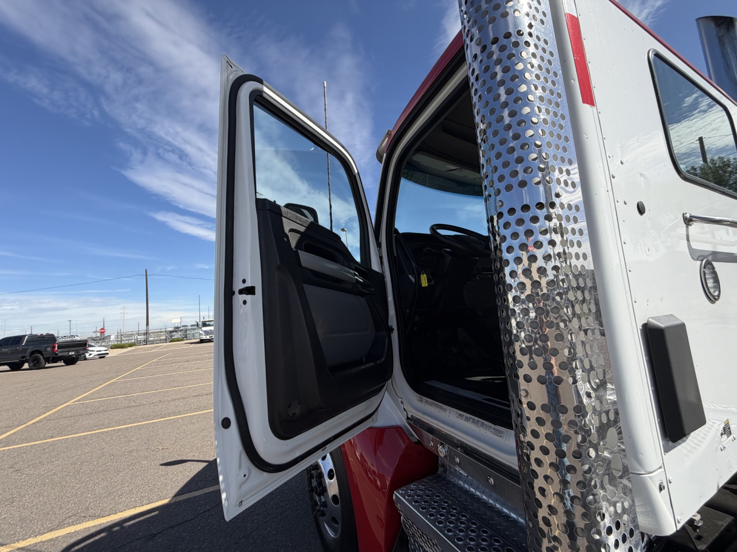 Truck cab interior visible with open door on a Kenworth T880, metal diamond-plate steps, and exterior chrome exhaust stack.