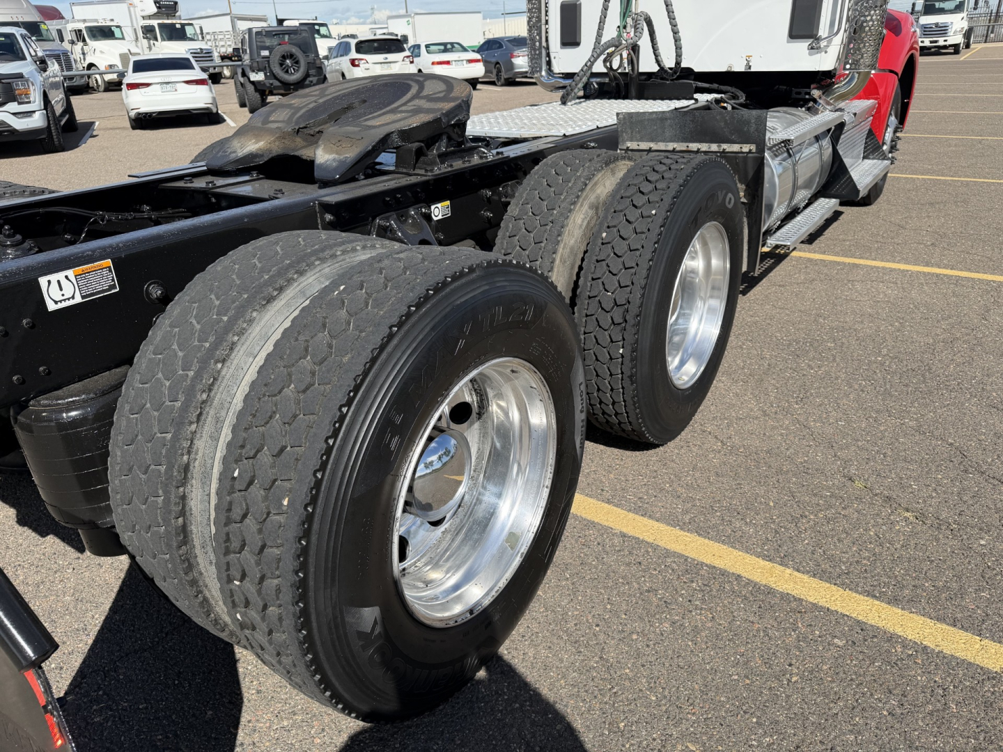 Kenworth T880 conventional daycab chassis showing dual rear axles and tires, cargo area, and part of cab in a parking lot.