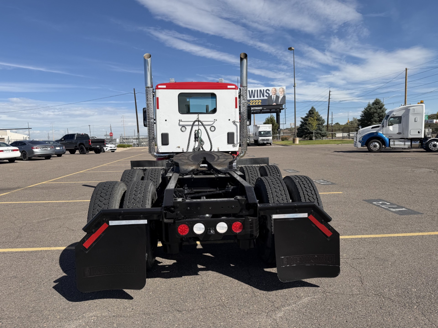 Truck chassis and cab rear view of a Kenworth T880 with twin vertical exhausts and mud flaps in a dealership lot.