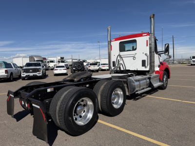 Kenworth T880 daycab tractor with red and white cab, dual rear axles, chassis, and fuel tanks in an outdoor lot.