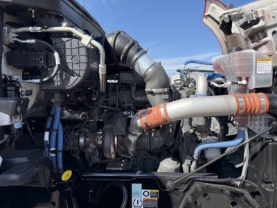 Truck engine bay of a 2023 Kenworth T880 with visible turbocharged engine, air intake, hoses, and electrical connections.