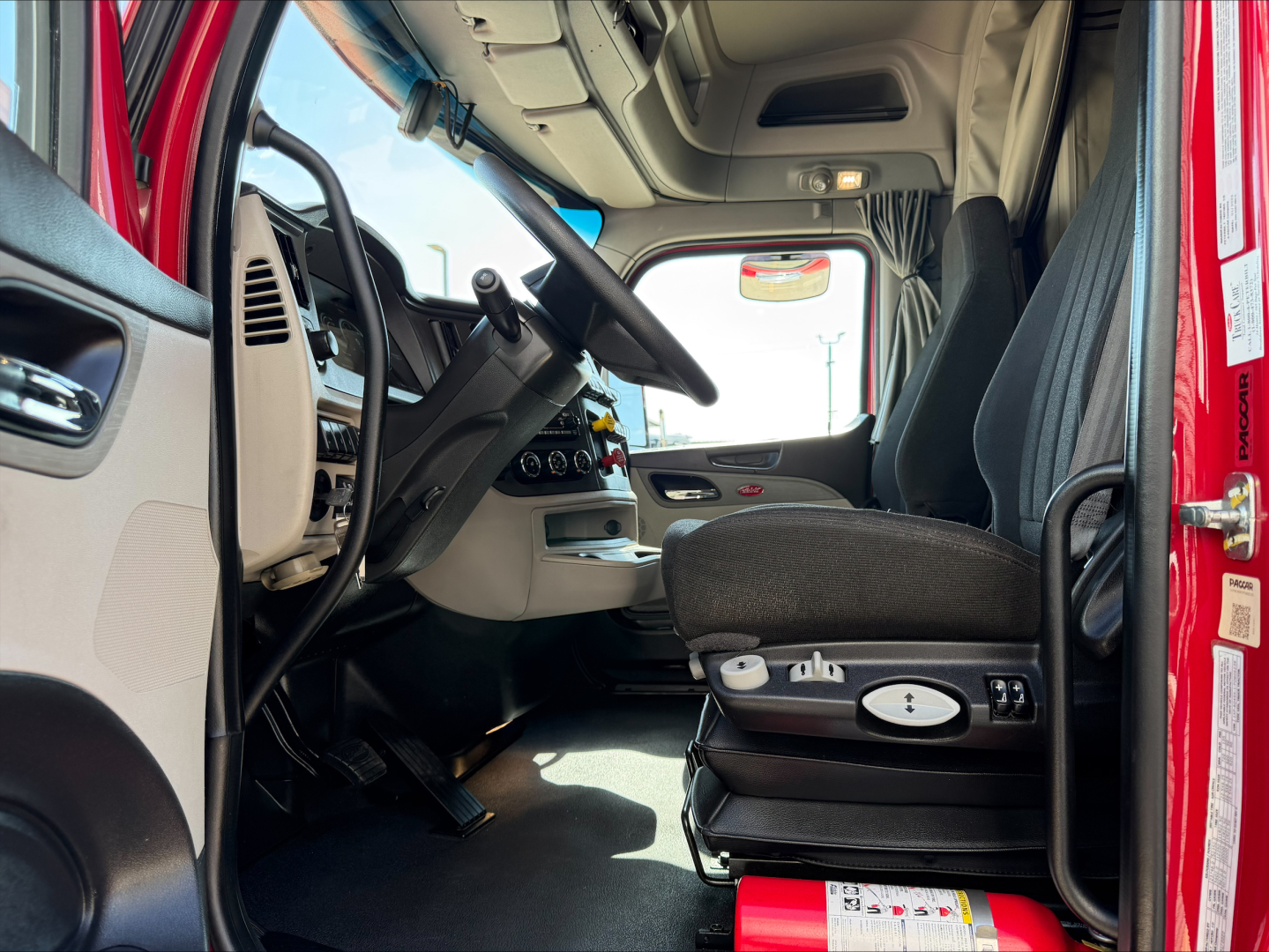 Truck cab interior of a 2023 Peterbilt 579 conventional sleeper showing driver's seat, steering wheel, dashboard, and door frame.