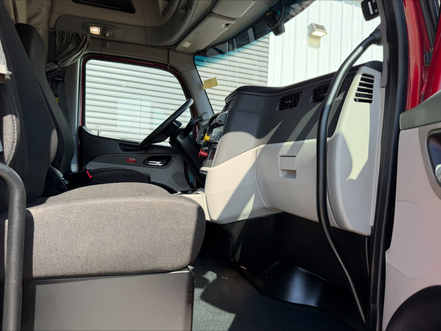Peterbilt 579 cab interior with driver's seat, dashboard, and steering wheel visible from passenger side; gray seats, light gray panels, center console, large windshield.