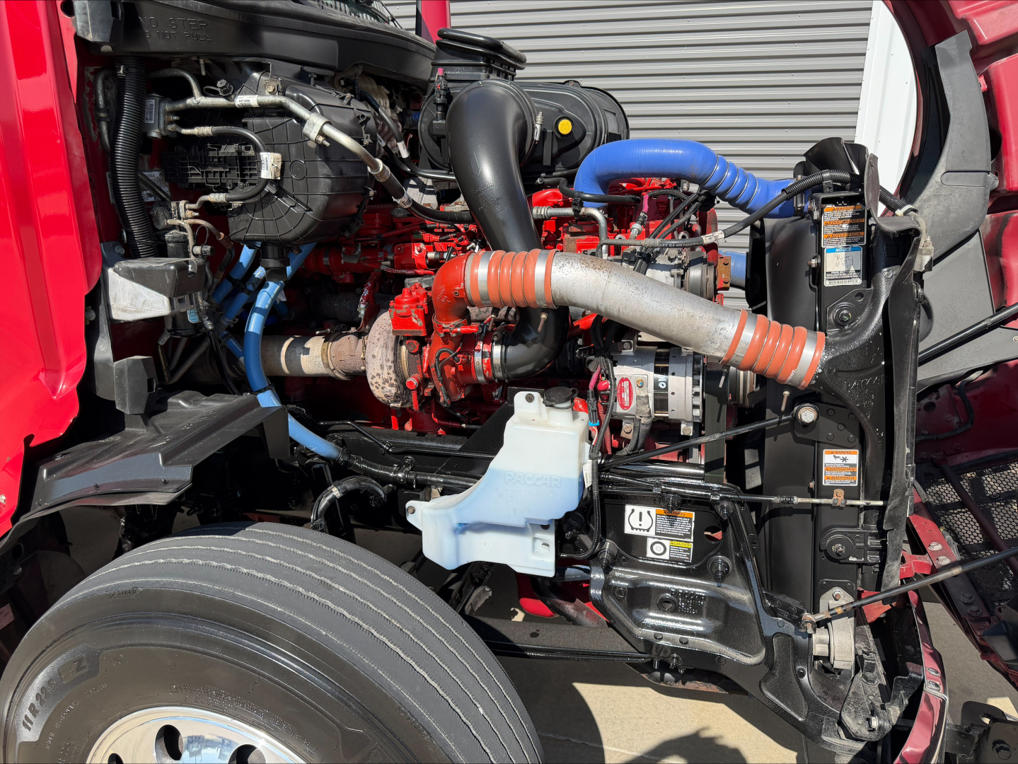 Peterbilt 579 engine bay showing turbo hoses, coolant reservoir, and various hoses and components visible in a red truck.
