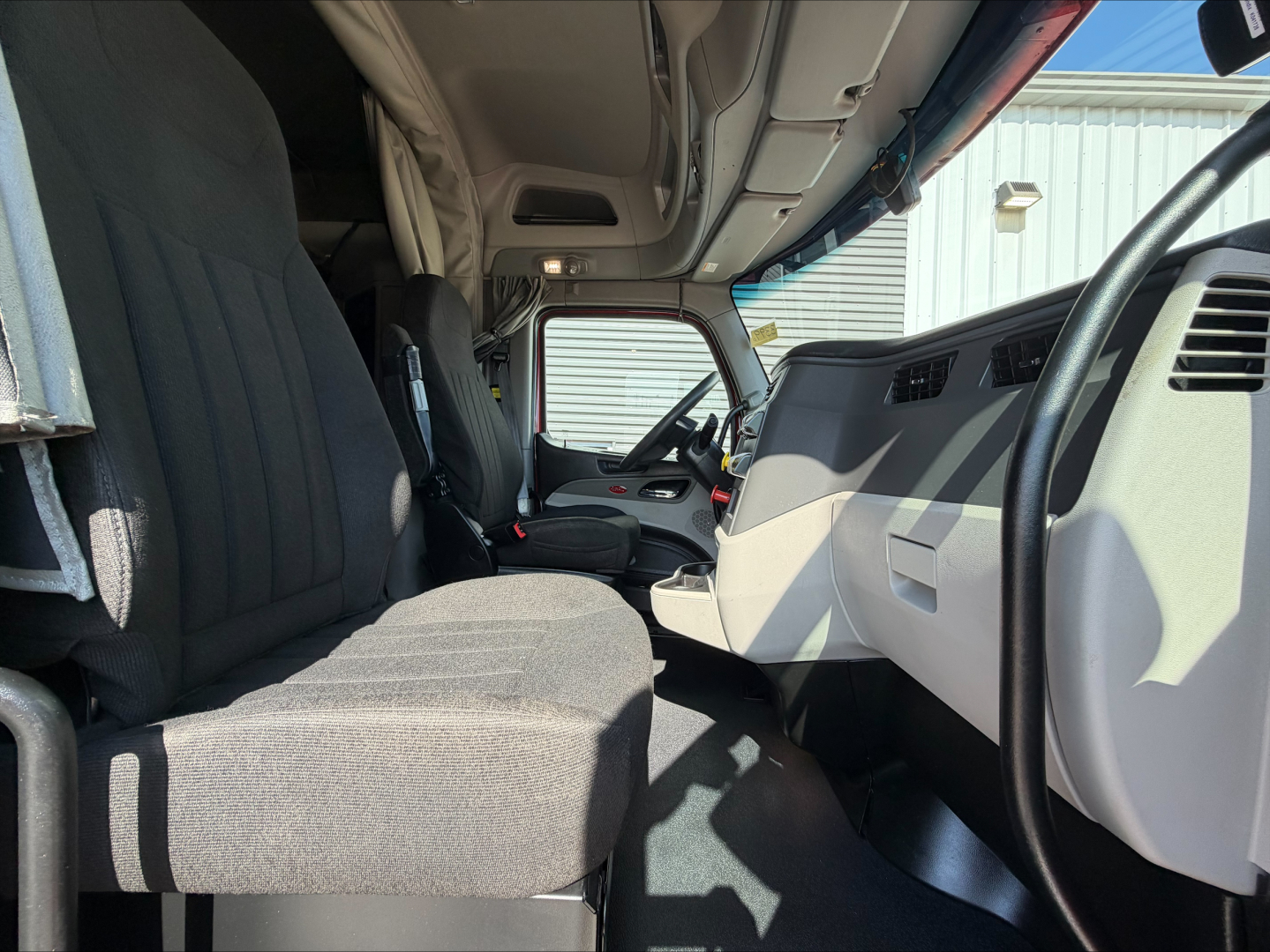 Interior cab of a 2023 Peterbilt 579 conventional sleeper truck showing front seats, dash, steering wheel, and overhead storage.