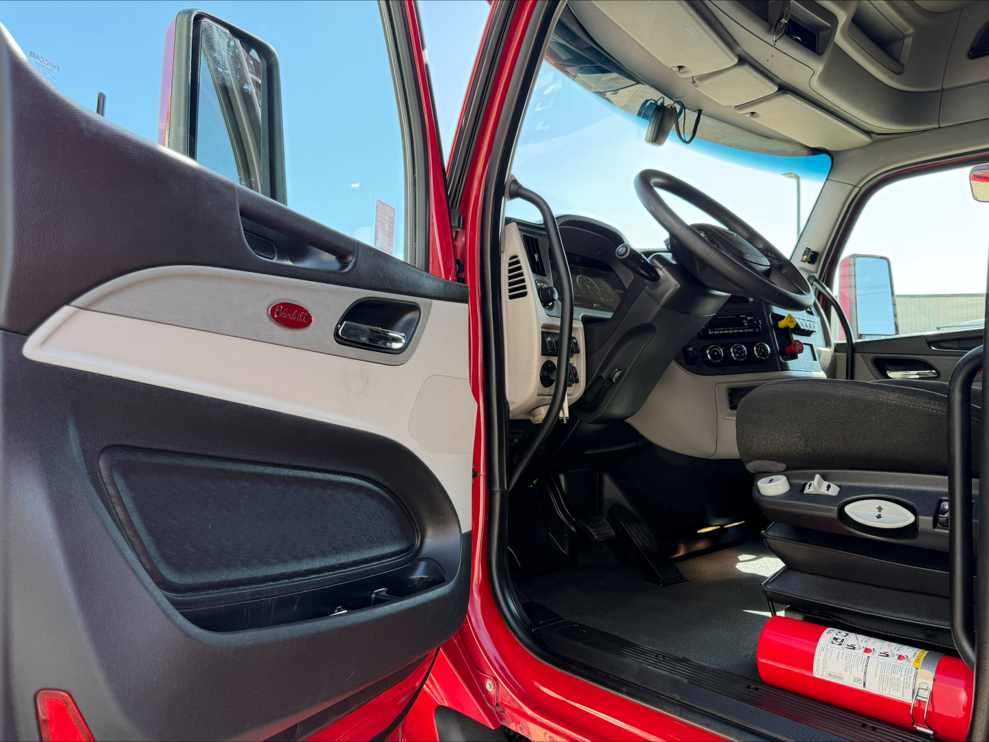 Peterbilt 579 interior cab view with open door showing steering wheel, dashboard, and red exterior