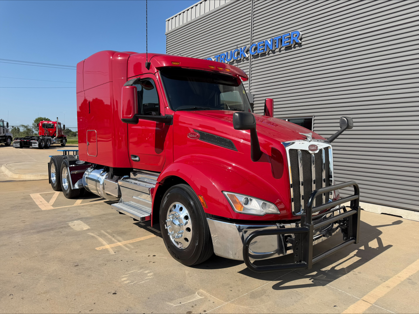 Peterbilt 579 truck in red showing front grille with bumper guard and chrome exhaust, applied on-day sun; side view reveals sleeper cab and dual rear axles.