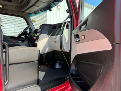 Peterbilt 579 cab interior view showing driver seat, dashboard, steering wheel, and open door with pink and gray door panel.