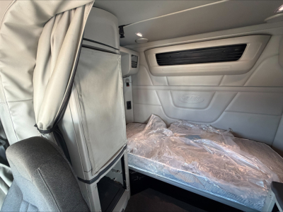 Peterbilt 579 sleeper cab interior showing side bunk bed with plastic-wrapped mattress and upper storage cabinet.