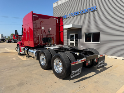 Peterbilt 579 tractor rear view showing dual rear axles, red cab, chrome fuel tanks, and fifth-wheel area; visible stock sign in background.