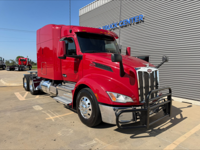 Peterbilt 579 truck in red showing front grille with bumper guard and chrome exhaust, applied on-day sun; side view reveals sleeper cab and dual rear axles.