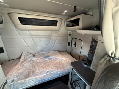 Peterbilt 579 sleeper cab interior showing front wall panels, overhead storage, and bed platform with plastic cover.