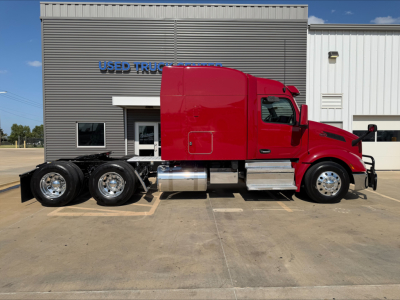 Peterbilt 579 sleeper cab tractor in red, side profile view, 3-axle with dual rear axles, parked in front of a used trucks building.