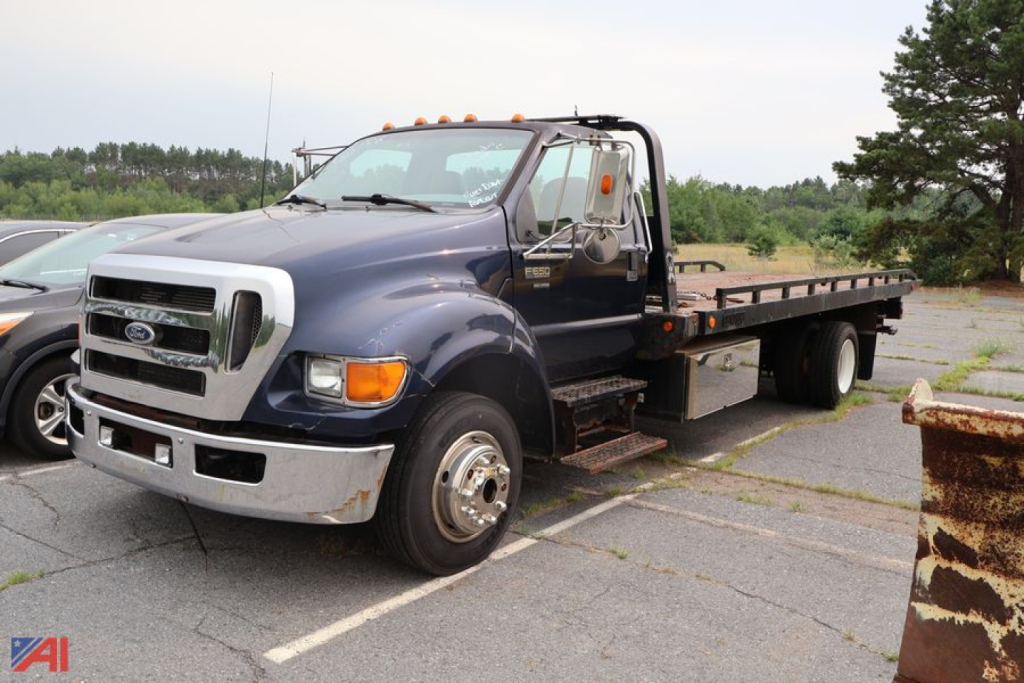 Ford F650 Super Duty cab and chassis truck in a parking lot with flatbed, side steps, and dual rear wheels.