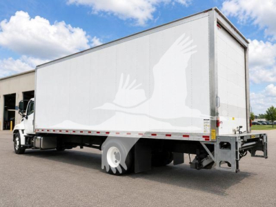 Box truck with white exterior and bird graphic on side, rear view shows trailer and cab with blue sky.