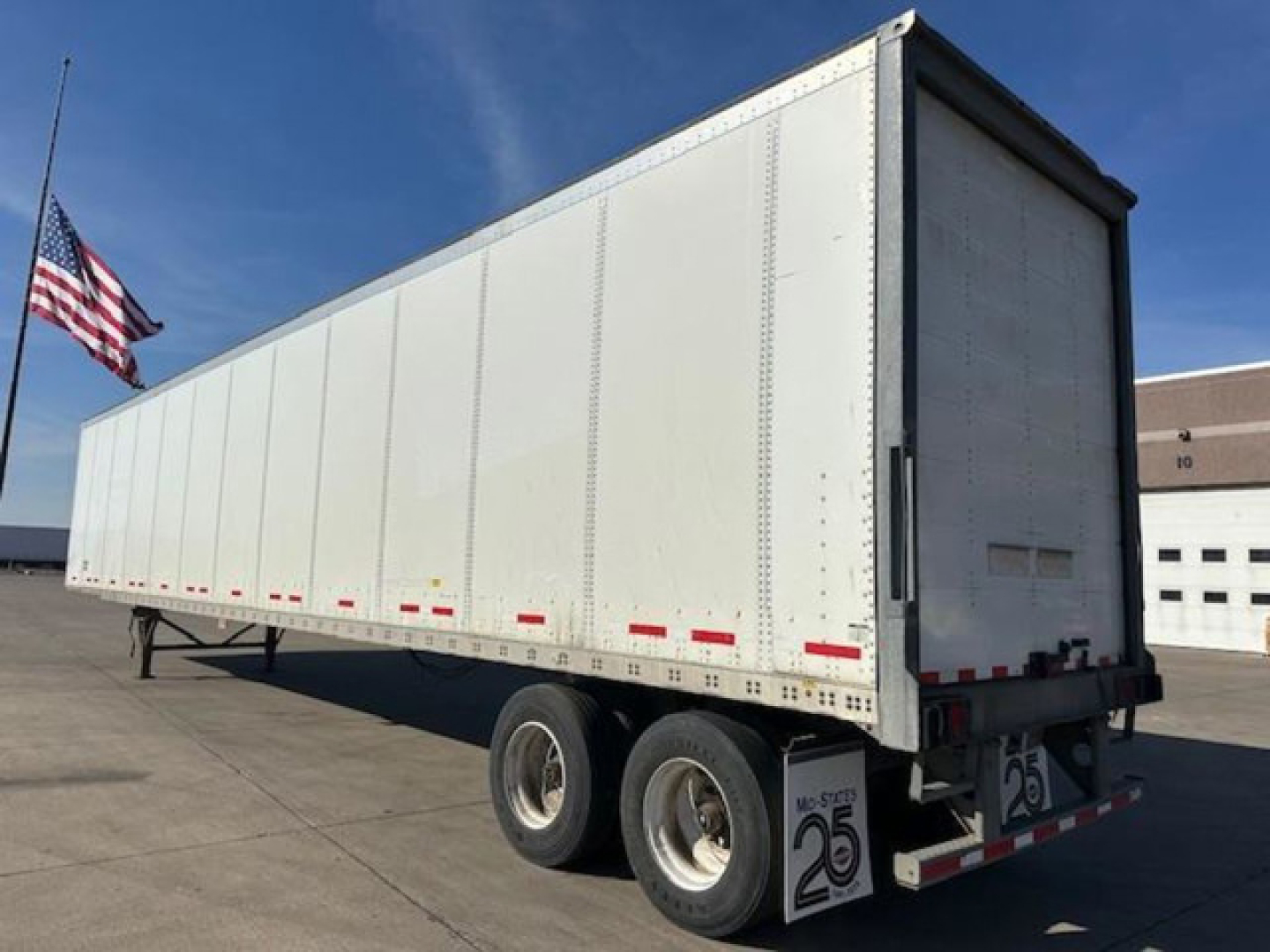Trailer side view showing a white Wabash van trailer with dual rear axles and rear doors; US flag in background.