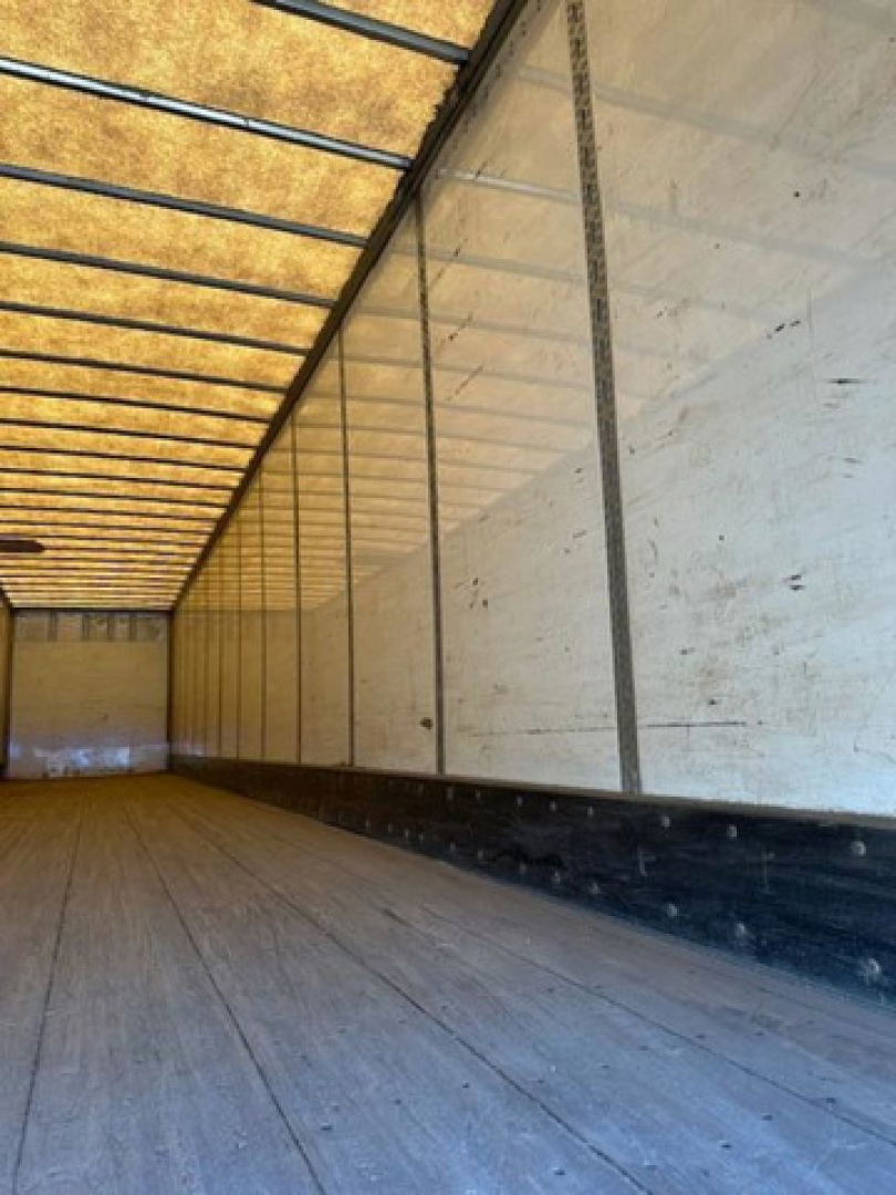 Trailer interior showing wooden floor and white side walls with ribbed metal supports.