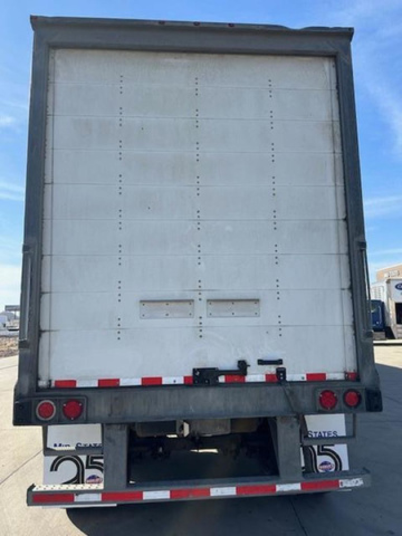 Rear view of a white Wabash trailer with vertical riveted panels, red and white reflective tape, taillights, and bumper.