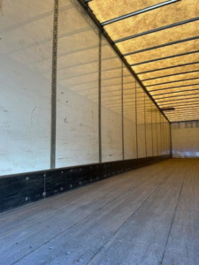 Van trailer interior showing wooden floor and side walls with vertical steel ribs and a high ceiling.