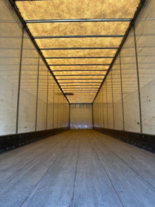 Trailer interior showing a long empty cargo area with wooden floor and light panels along the ceiling.